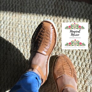 Pu&ograve; includere: Un paio di sandali in pelle marrone con cinturini intrecciati. Le sandali sono indossate da una persona che indossa jeans blu. Le sandali sono su un tappeto intrecciato. L'immagine include il testo "Magical Mexico Artisanal Boutique Huaraches Clothing Accessories".