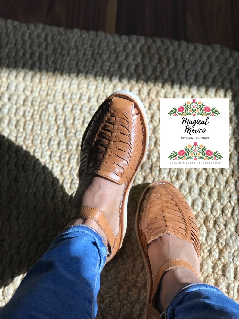 Pu&ograve; includere: Un paio di sandali in pelle marrone con cinturini intrecciati. Le sandali sono indossate da una persona che indossa jeans blu. Le sandali sono su un tappeto intrecciato. L'immagine include il testo "Magical Mexico Artisanal Boutique Huaraches Clothing Accessories".