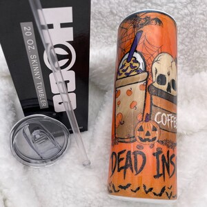 Może przedstawiać: Kubek skinny o pojemności 20 uncji z wzorem w stylu Halloween. Kubek przedstawia kubek do kawy z czaszką, nietoperzami i dyniami. Na kubku nadrukowany jest tekst "Dead Inside" i "Coffee".