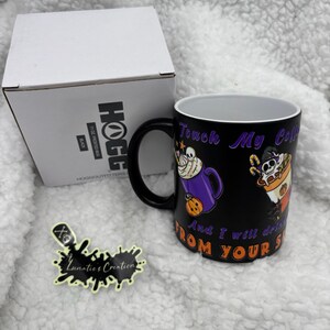 May include: Black ceramic mug with a Halloween-themed design. The mug features the text "Touch My Coffee And I will drink from your soul" with illustrations of a skull and a pumpkin. A white box and a sticker are also in the image.
