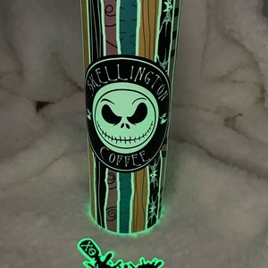 Op de afbeelding: Een glow-in-the-dark tumbler met een zwart-wit ontwerp met Jack Skellington uit The Nightmare Before Christmas. De tumbler heeft een zwarte cirkel met de tekst "Skellington Coffee" en een afbeelding van Jack Skellingtons gezicht. De tumbler is omgeven door een witte achtergrond.