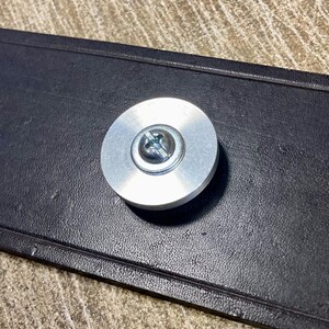 Peut inclure: Gros plan d'un objet m&eacute;tallique circulaire argent&eacute; avec une vis au centre, fix&eacute; &agrave; une pi&egrave;ce rectangulaire noire. L'objet m&eacute;tallique a une finition bross&eacute;e.