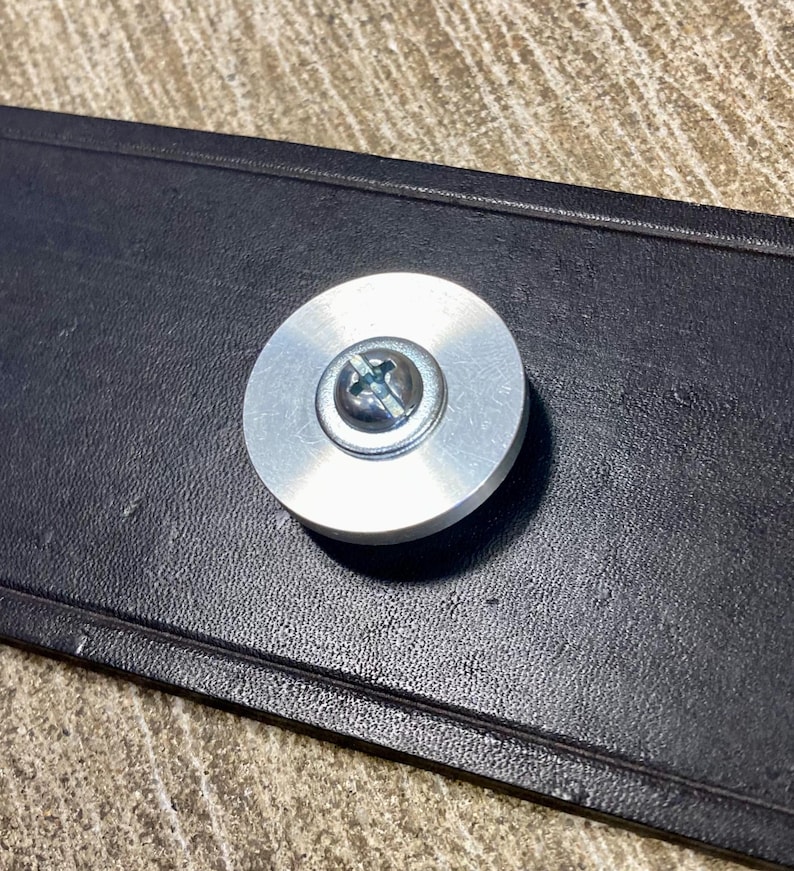 Peut inclure: Gros plan d'un objet m&eacute;tallique circulaire argent&eacute; avec une vis au centre, fix&eacute; &agrave; une pi&egrave;ce rectangulaire noire. L'objet m&eacute;tallique a une finition bross&eacute;e.