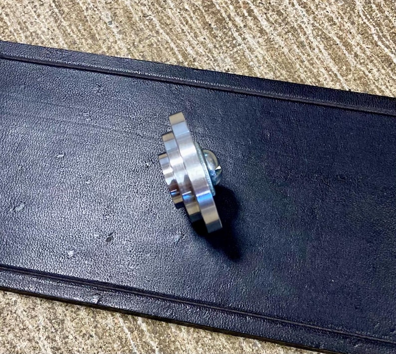 Peut inclure: Un objet m&eacute;tallique argent&eacute; brillant en forme d'&eacute;toile, avec plusieurs pointes et une vis centrale. L'objet est pos&eacute; sur un fond sombre et textur&eacute;, peut-&ecirc;tre du cuir ou un mat&eacute;riau similaire.