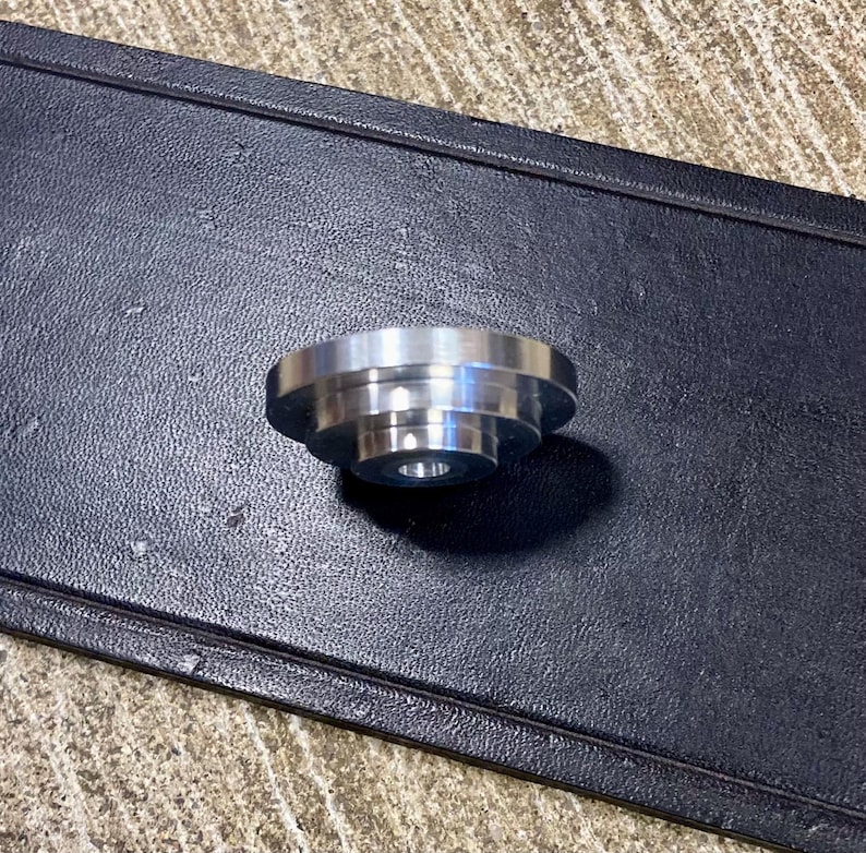 Peut inclure: Un petit composant m&eacute;tallique argent&eacute; avec un design &eacute;tag&eacute;. Le composant a une forme circulaire avec un trou central et repose sur une surface noire textur&eacute;e.