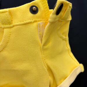 May include: Yellow denim shorts with a cuffed hem and a button closure. The shorts are unzipped and the fabric is textured.