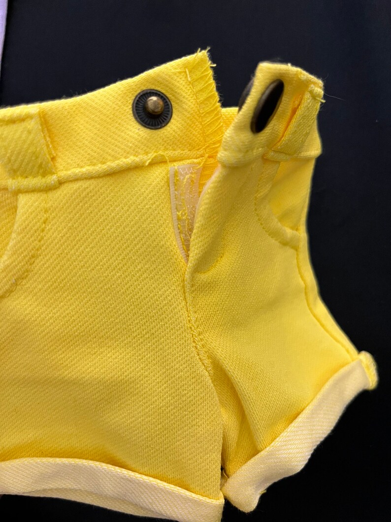May include: Yellow denim shorts with a cuffed hem and a button closure. The shorts are unzipped and the fabric is textured.