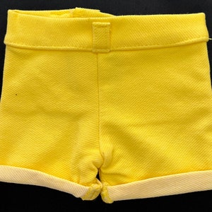 May include: A pair of yellow shorts with a cuffed hem. The shorts are made of a textured fabric.