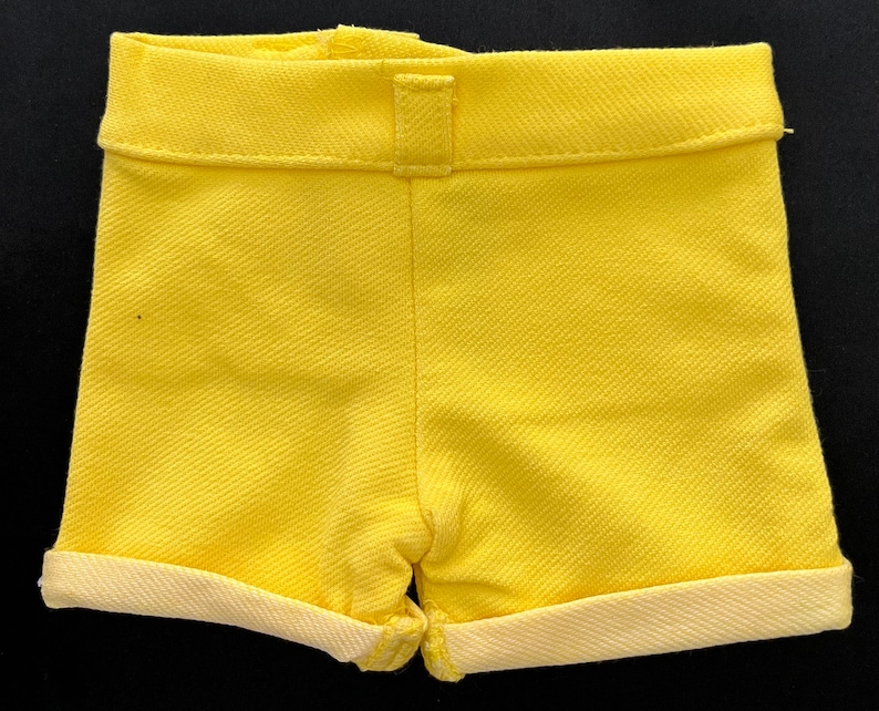 May include: A pair of yellow shorts with a cuffed hem. The shorts are made of a textured fabric.