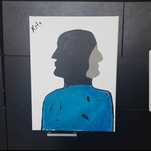 May include: A painting of a person with two faces, one black and one gray, against a white background. The person is wearing a blue shirt. The painting is signed "Kota" in the top left corner.