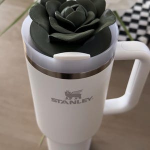 Peut inclure: Une tasse en c&eacute;ramique blanche avec une anse noire et le texte "But First, Coffee" dans un style manuscrit. La tasse est pos&eacute;e sur une surface blanche. La tasse mesure 10 cm de haut.