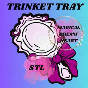 Op de afbeelding: Een decoratief sieradenbakje met de tekst "TRINKET TRAY" bovenaan. De bak is wit met een roze en zwarte omtrek, een roze strik en de tekst "STL" onderaan. De woorden "MAGICAL DREAM HEART" staan in een gouden cirkel.