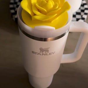 Peut inclure: Mug Stanley blanc avec un couvercle en forme de rose jaune et une poign&eacute;e blanche. Le logo Stanley est imprim&eacute; sur le devant. Une paille blanche est ins&eacute;r&eacute;e dans le couvercle. Le mug est con&ccedil;u pour les boissons chaudes ou froides.