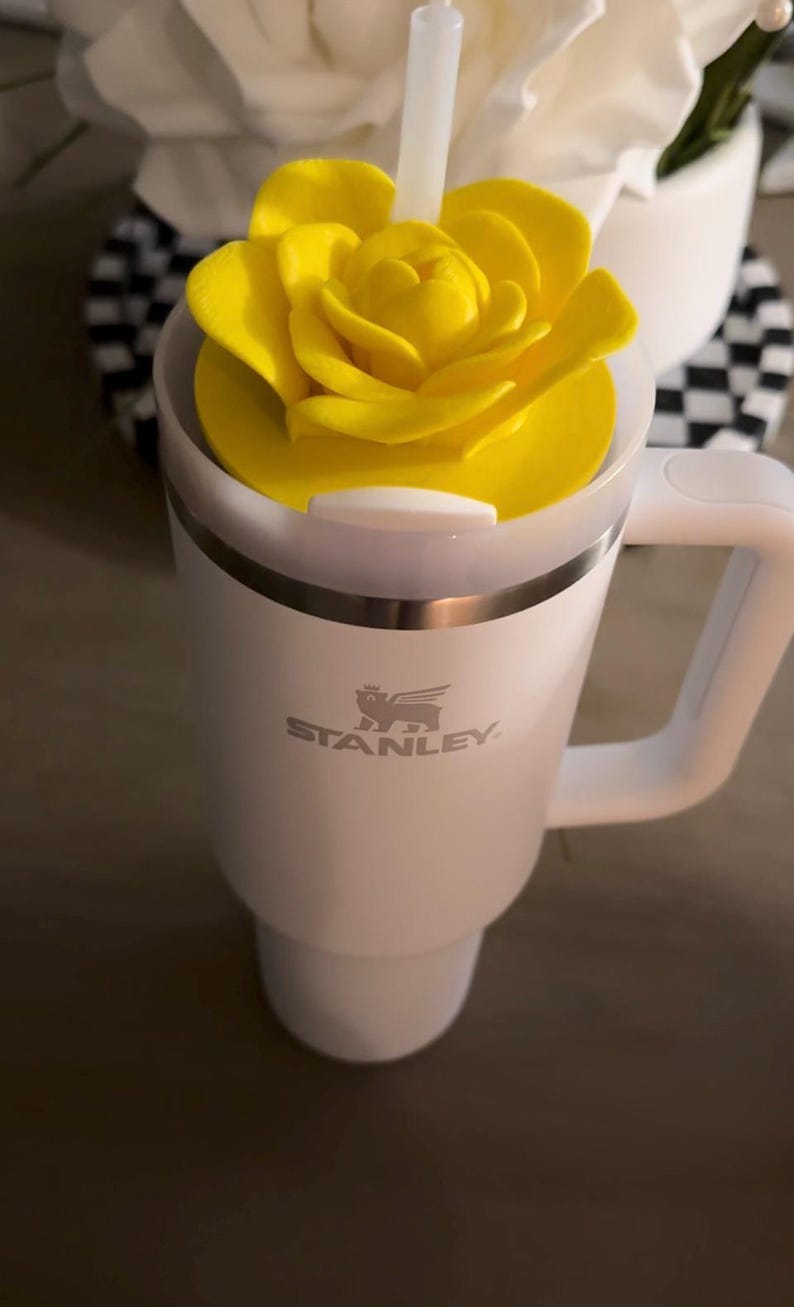 Peut inclure: Mug Stanley blanc avec un couvercle en forme de rose jaune et une poign&eacute;e blanche. Le logo Stanley est imprim&eacute; sur le devant. Une paille blanche est ins&eacute;r&eacute;e dans le couvercle. Le mug est con&ccedil;u pour les boissons chaudes ou froides.