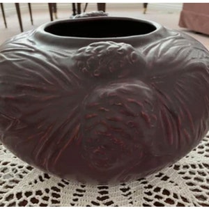 May include: A dark brown ceramic vase with a textured, floral design. The vase has a wide opening and a rounded shape.