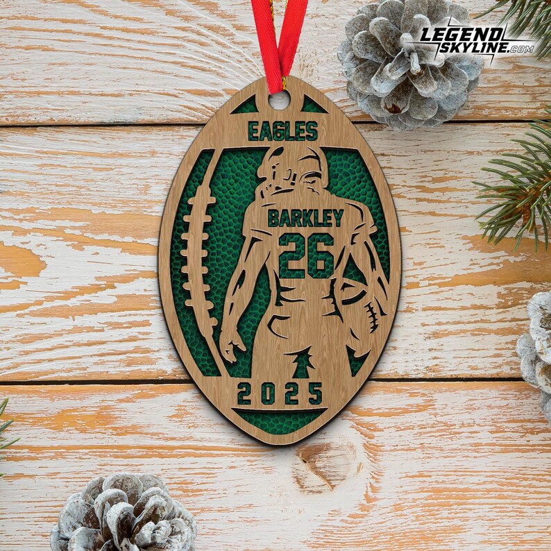 May include: Wooden football-shaped ornament with a green interior and a player silhouette. The ornament features the word "EAGLES" at the top, "BARKLEY 26" in the center, and "2025" at the bottom. A red ribbon is attached for hanging.