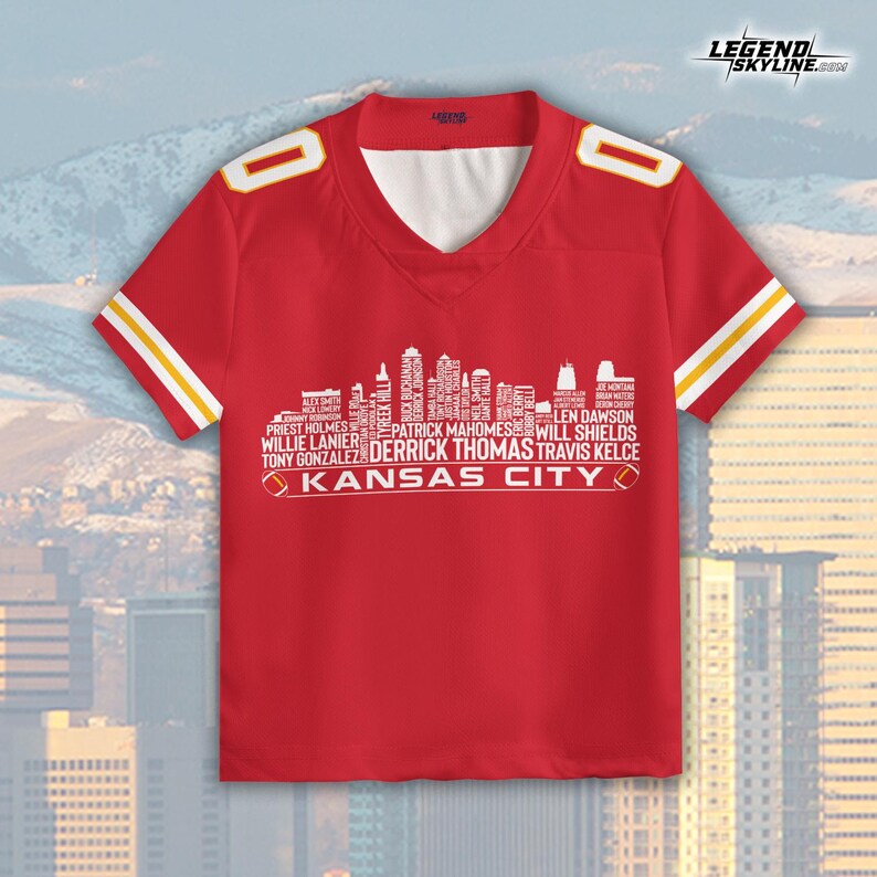 Puede incluir: Camiseta de f&uacute;tbol roja con detalles blancos y amarillos. La camiseta presenta un gr&aacute;fico de horizonte blanco con nombres de jugadores y el texto "KANSAS CITY". Tiene cuello en V y mangas cortas.