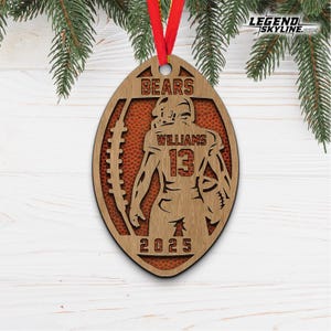 May include: Wooden football-shaped ornament with a football player design. The ornament features the word "BEARS" at the top, the name "WILLIAMS" and the number "13". The year "2025" is at the bottom. A red ribbon is attached for hanging.