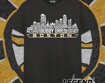 May include: Black t-shirt with a white graphic of the Boston skyline. The skyline is made up of the names of famous Boston Bruins hockey players, including Bobby Orr, Ray Bourque, and Cam Neely. The text "BOSTON" is written in yellow at the bottom of the graphic.