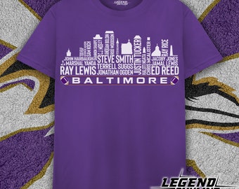 May include: Purple t-shirt with a white graphic of the Baltimore Ravens team logo. The logo is made up of the names of famous players, including Ray Lewis, Terrell Suggs, and Ed Reed. The text "Baltimore" is at the bottom of the graphic.