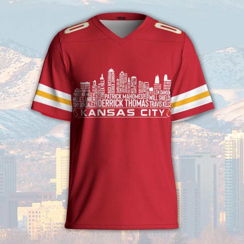 May include: Red football jersey with white and yellow stripes on the sleeves. The jersey features a white skyline graphic with player names and the text "KANSAS CITY". The jersey has a V-neck and the number "0" on the shoulders.