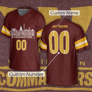 May include: A burgundy V-neck jersey with gold and white sleeve stripes. The front features a white Washington skyline graphic with names, the text WASHINGTON, and the number 00. The back displays the number 00 in gold with white outlines.