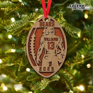 May include: Wooden football-shaped Christmas ornament with a red ribbon. The ornament features a football player silhouette, the name "WILLIAMS" and the number "13". The word "BEARS" is at the top, and "2025" at the bottom.