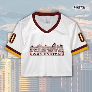 Peut inclure: Maillot court blanc avec un col en V et des bordures de manches bordeaux, portant le chiffre "0" sur les manches. Le devant affiche un graphique de skyline avec des noms de joueurs et le mot "WASHINGTON". Le logo Legend Skyline est en haut &agrave; droite.