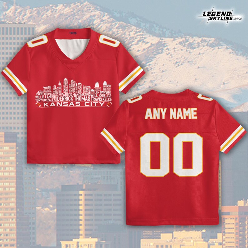 Puede incluir: Camiseta roja con rayas blancas y amarillas. La parte delantera presenta un gr&aacute;fico de horizonte blanco con nombres de jugadores y "KANSAS CITY". La parte trasera tiene "ANY NAME" encima del n&uacute;mero "00".