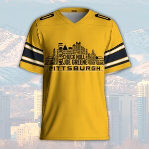 May include: A yellow V-neck jersey with black and white stripes on the sleeves. The jersey features a black silhouette of a city skyline with the word "PITTSBURGH" and names of famous players.