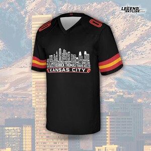 Puede incluir: Camiseta de f&uacute;tbol negra con detalles rojos y amarillos. La camiseta presenta un gr&aacute;fico de horizonte blanco con nombres de jugadores y el texto "KANSAS CITY". El n&uacute;mero "0" se muestra en los hombros.