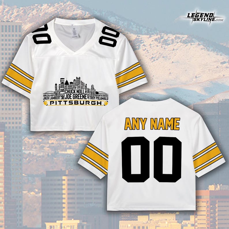 May include: White football jersey with black and gold accents. The front features a Pittsburgh skyline graphic and player names. The back has "ANY NAME" and the number "00". The jersey has a V-neck and short sleeves.