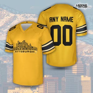May include: A yellow football jersey with black and white stripes on the sleeves. The front features a Pittsburgh skyline graphic with player names. The back displays "ANY NAME" above the number "00".
