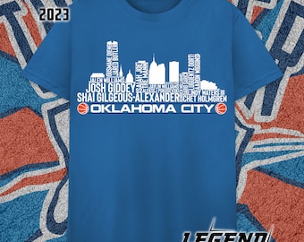 Może przedstawiać: Koszulka w kolorze królewskiego błękitu z białą sylwetką panoramy Oklahoma City. Panorama składa się z nazwisk koszykarzy Oklahoma City Thunder z sezonu 2023. Pod panoramą widnieje napis "Oklahoma City" z piłką do koszykówki po obu stronach.