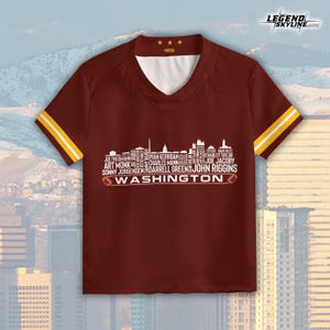 Peut inclure: Maillot bordeaux &agrave; col en V avec des accents blancs et dor&eacute;s. Le maillot pr&eacute;sente un graphisme de skyline blanc avec des noms de joueurs et le mot "WASHINGTON" en blanc. Les manches ont des rayures dor&eacute;es. Le coin sup&eacute;rieur droit porte le texte "LEGEND SKYLINE".