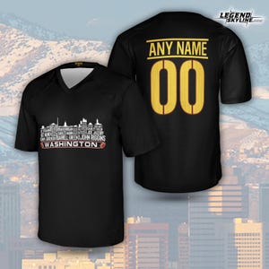 Peut inclure: Maillot noir &agrave; col en V avec un graphique de skyline et le mot "WASHINGTON". Le dos du maillot porte le texte "ANY NAME" au-dessus du num&eacute;ro "00" en or. Le maillot est un t-shirt de sport &agrave; manches courtes.