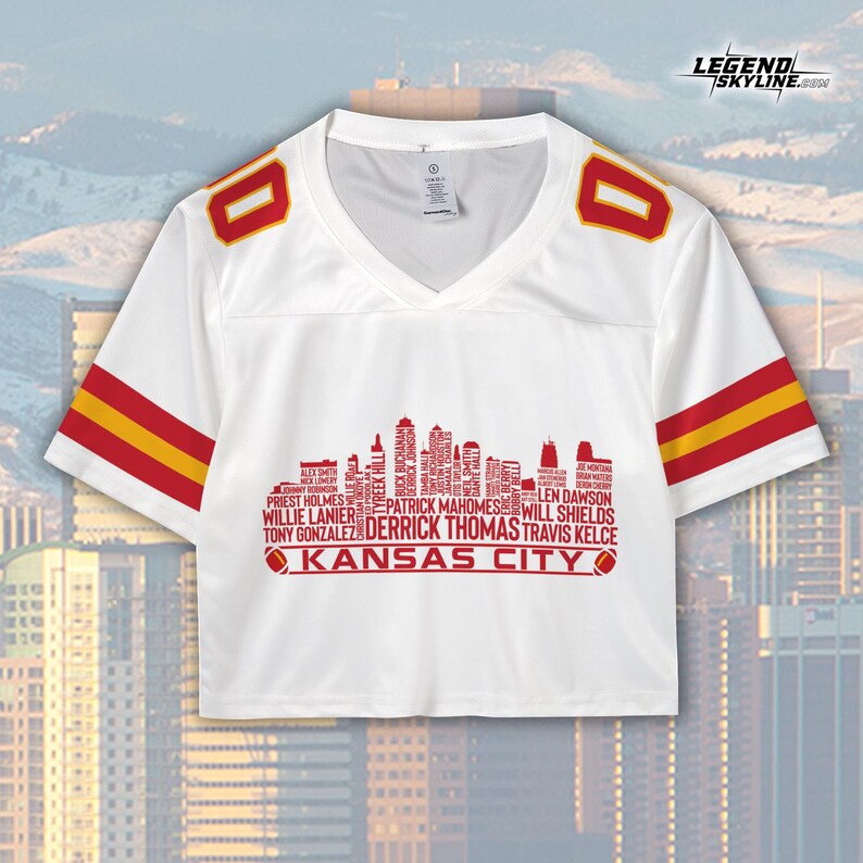 May include: White crop top jersey with red and yellow accents. The jersey features the number "0" on the shoulders and red and yellow stripes on the sleeves. A red skyline graphic with player names and "KANSAS CITY" is printed on the front.