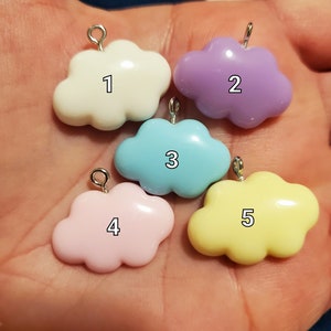 May include: Five cloud-shaped charms in various pastel colors: white, lavender, light blue, pink, and yellow. Each charm has a silver-colored loop at the top for attaching to jewelry or other crafts. Numbers 1 through 5 are printed on each cloud.