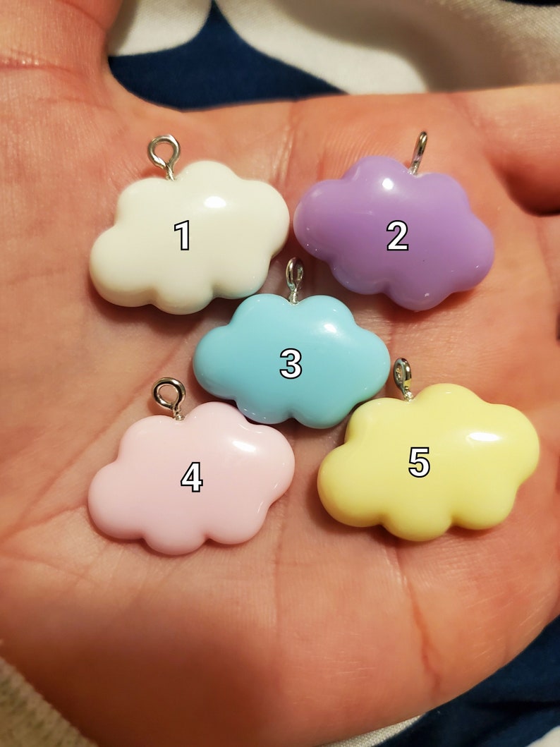 May include: Five cloud-shaped charms in various pastel colors: white, lavender, light blue, pink, and yellow. Each charm has a silver-colored loop at the top for attaching to jewelry or other crafts. Numbers 1 through 5 are printed on each cloud.
