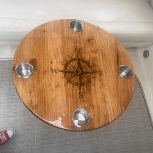 May include: A round wooden table with a compass design and four cup holders. The table is made of light brown wood and has a glossy finish.