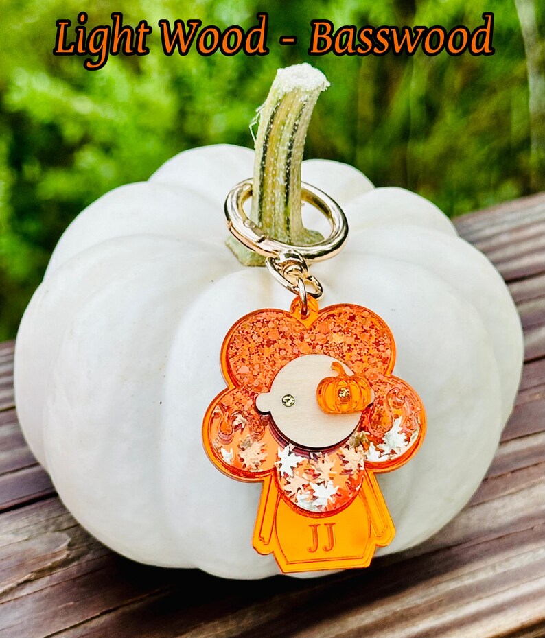May include: Orange and white glitter pumpkin charm with a wood face and the initials "JJ" on a gold key chain. The charm is hanging from a white pumpkin.