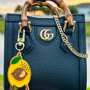 May include: Black leather handbag with bamboo handles and a gold chain strap. The bag has a gold GG logo on the front and a lemon-shaped keychain.