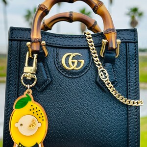 May include: A black leather handbag with bamboo handles and a gold chain strap. The bag has a gold GG logo on the front and a lemon-shaped keychain.