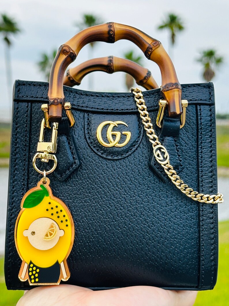 May include: A black leather handbag with bamboo handles and a gold chain strap. The bag has a gold GG logo on the front and a lemon-shaped keychain.