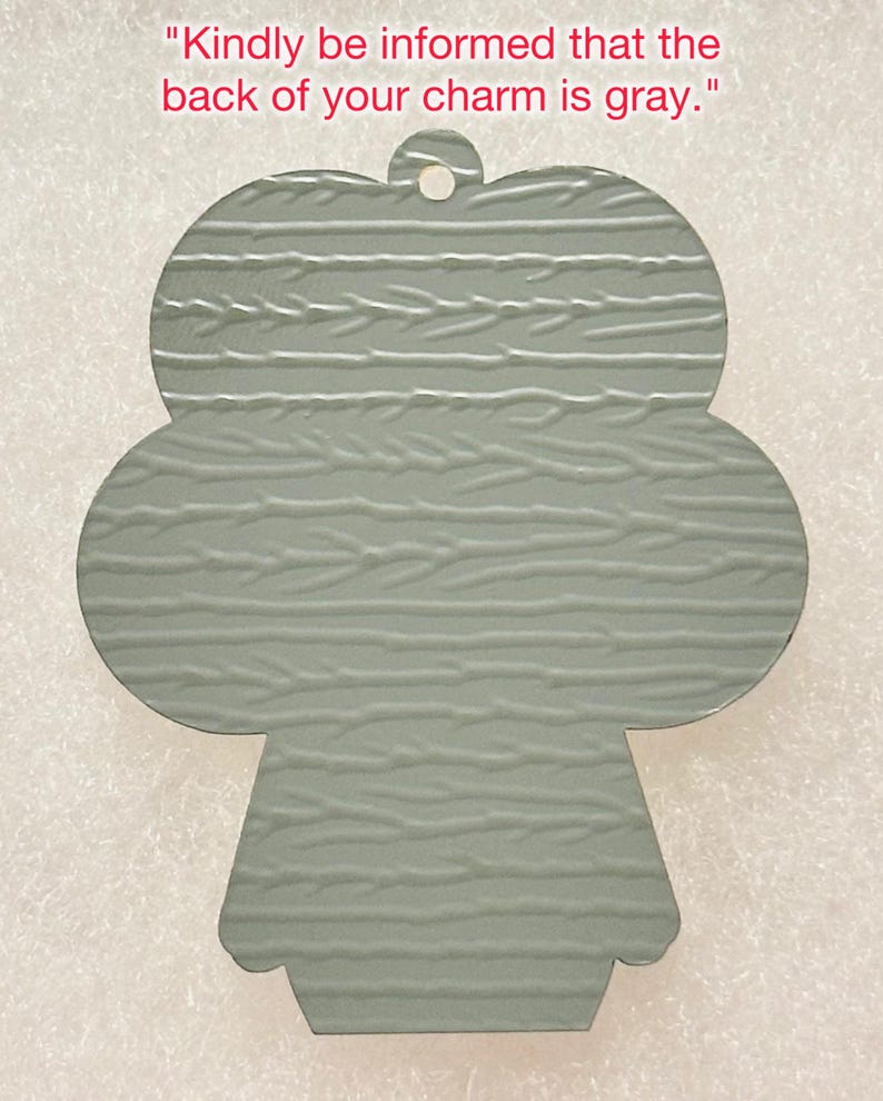May include: A gray metal charm in the shape of a clover with a textured surface. The back of the charm is gray.