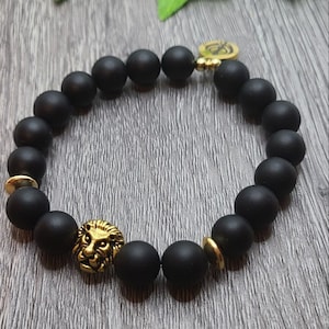 Puede incluir: Pulsera de cuentas negras con detalles de cabeza de león dorados.