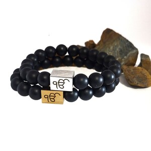 Peut inclure: Deux bracelets en perles noires avec des breloques dorées et argentées représentant le symbole "ੴ".
