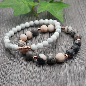 Puede incluir: Dos pulseras hechas de cuentas de mármol blanco y rosa con detalles en oro rosa. Las pulseras están apiladas una encima de la otra.