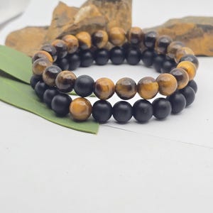 Könnte beinhalten: Zwei Perlenarmbänder, eines mit schwarzen Perlen und eines mit Tigerauge-Perlen.