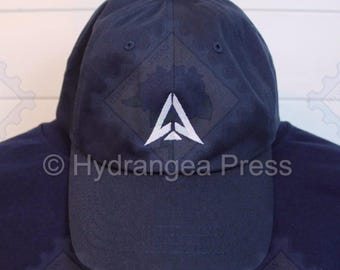 May include: A navy blue baseball cap with a white embroidered triangle logo. The logo has a stylized letter "A" inside the triangle.
